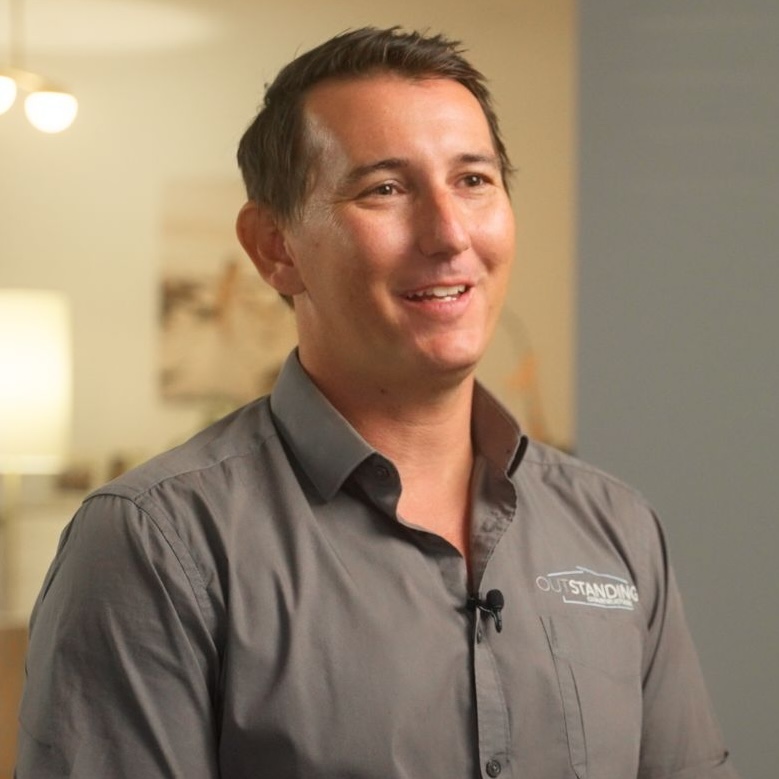 Jamie Standing with a friendly smile, wearing a business suit, against a light background.